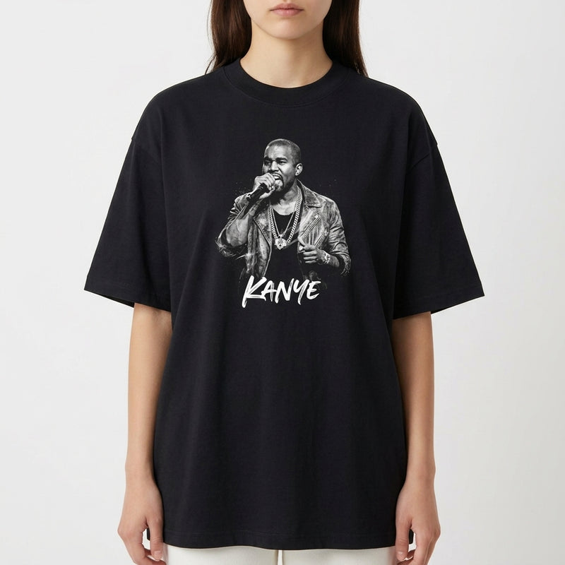 Camiseta com estampa frontal de um cantor segurando um microfone, vestindo jaqueta e colares, acompanhada pelo nome "Kanye" estilizado abaixo.