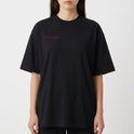 Camiseta com estampa frontal de inscrição estilizada e estampa traseira de urso sorridente com olhos em forma de "X" sobre fundo de respingos vibrantes.