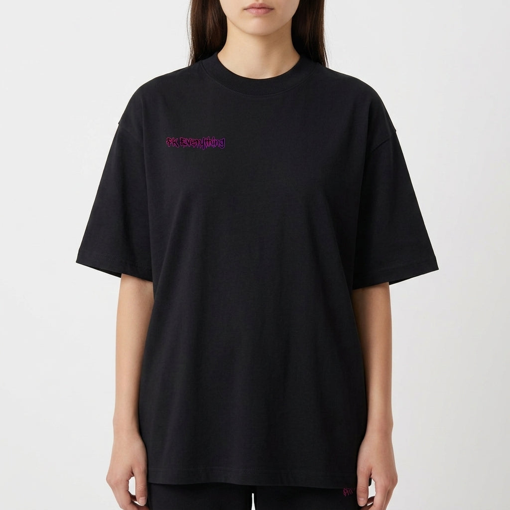 Camiseta com estampa frontal de inscrição estilizada e estampa traseira de urso sorridente com olhos em forma de "X" sobre fundo de respingos vibrantes.