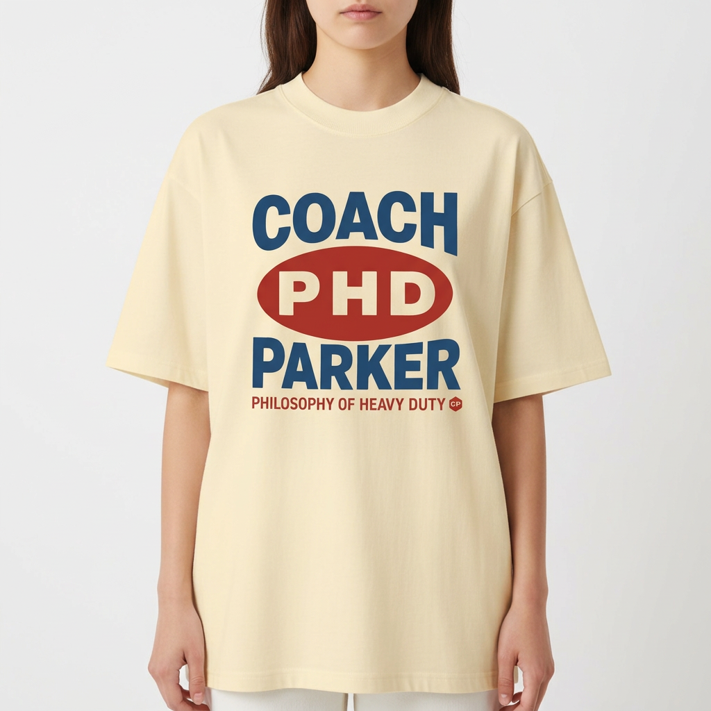 Camiseta com estampa frontal de texto estilizado com palavras "COACH PHD PARKER" em destaque, acompanhada de "PHILOSOPHY OF HEAVY DUTY" em menor tamanho.