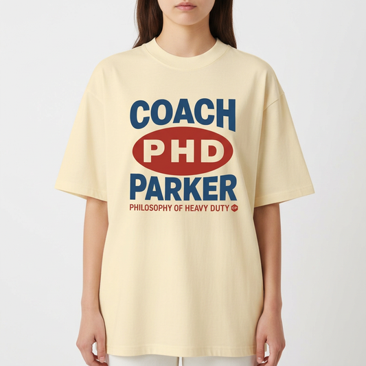 Camiseta com estampa frontal de texto estilizado com palavras "COACH PHD PARKER" em destaque, acompanhada de "PHILOSOPHY OF HEAVY DUTY" em menor tamanho.