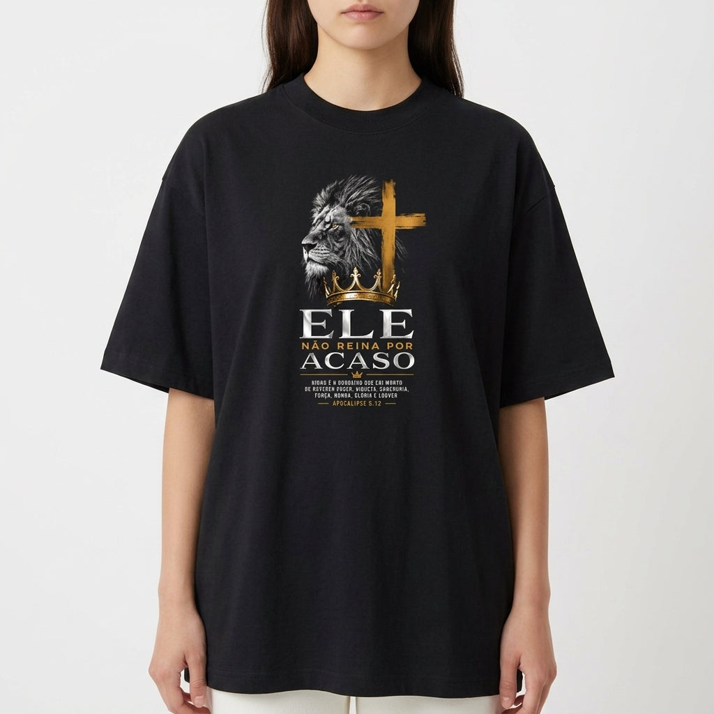 Camiseta com estampa frontal de leão em perfil ao lado de uma cruz, seguida pela frase "Ele não reina por acaso" e texto menor detalhando uma passagem.