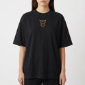 Camiseta com estampa frontal de símbolo estilizado minimalista e estampa traseira de personagem em pose dinâmica cercado por textos e gráficos detalhados.