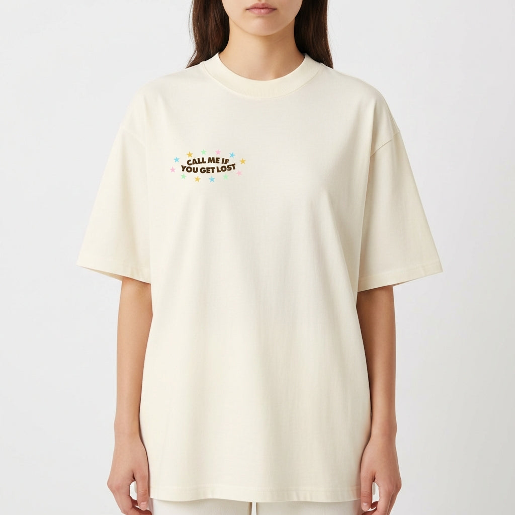 Camiseta com estampa frontal de texto "CALL ME IF YOU GET LOST" adornado com pequenas estrelas coloridas e estampa traseira de ilustração com figura relaxando em mala.