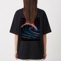 Camiseta com estampa frontal de pequeno texto no canto inferior e estampa traseira de onda imponente e sol vibrante em fundo quadriculado.