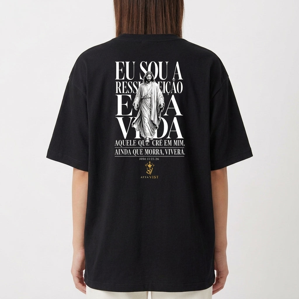 Camiseta com estampa traseira de uma figura central religiosa e frase que menciona ressurreição e vida, cercada por texto estilizado.