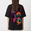 Camiseta com estampa frontal de círculo minimalista e estampa traseira de retrato feminino artístico em tons vibrantes com palmeiras e pôr do sol ao fundo.