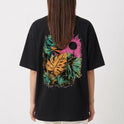 Camiseta com estampa frontal de pequeno logotipo minimalista e estampa traseira de folhas tropicais em diversas cores e círculo texturizado.