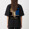 Camiseta com estampa frontal de logotipo minimalista e estampa traseira de prancha de surf encostada em parede desgastada com palmeira e fundo geométrico.