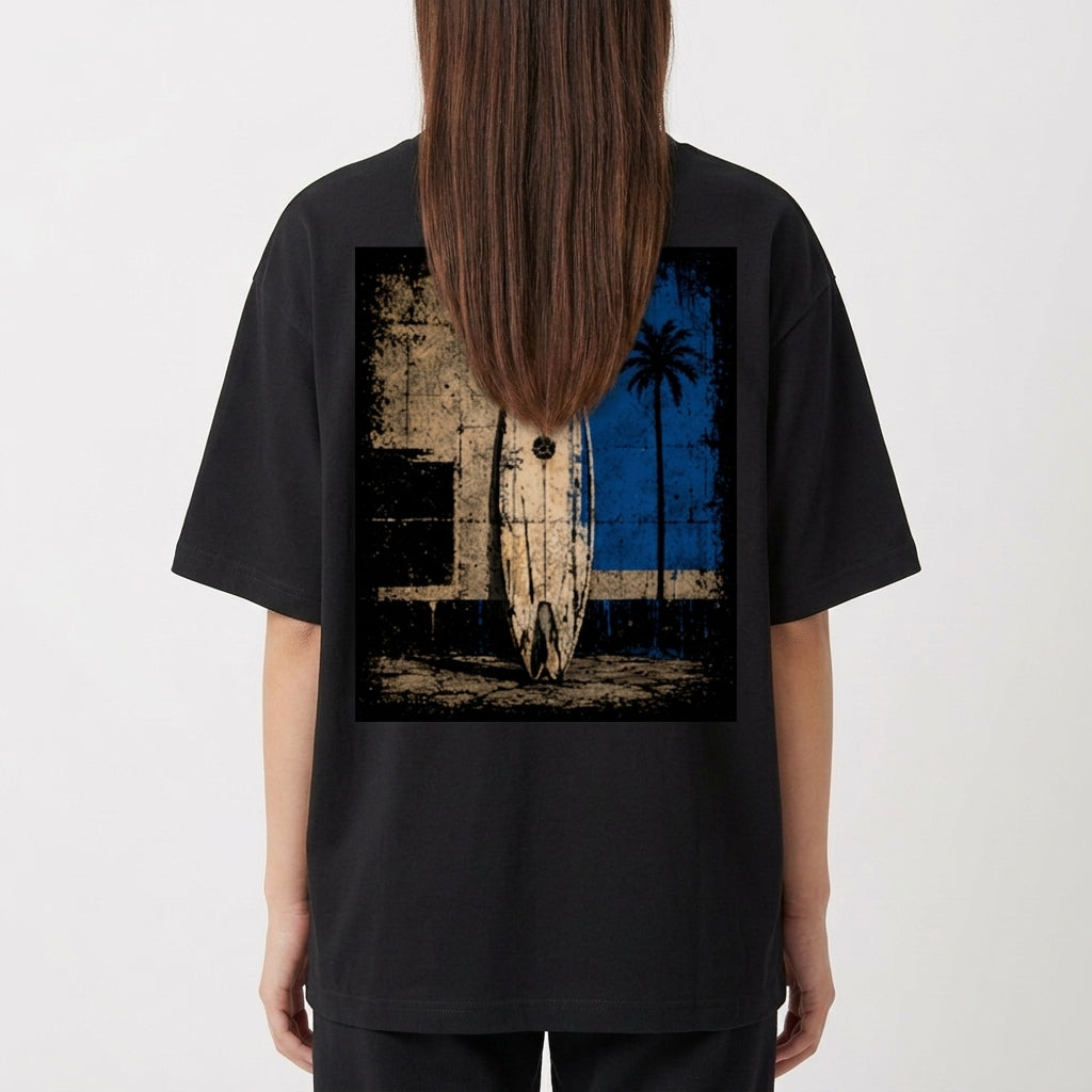 Camiseta com estampa frontal de logotipo minimalista e estampa traseira de prancha de surf encostada em parede desgastada com palmeira e fundo geométrico.
