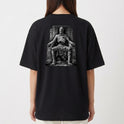 Camiseta com estampa frontal de logotipo estilizado com ornamentos e estampa traseira de figura esquelética sentada em um trono com detalhes rústicos.