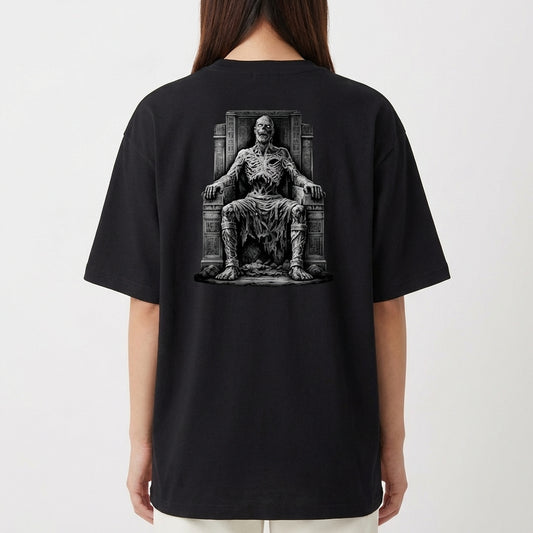 Camiseta com estampa frontal de logotipo estilizado com ornamentos e estampa traseira de figura esquelética sentada em um trono com detalhes rústicos.