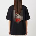 Camiseta com estampa frontal de texto estilizado em caixa vermelha e estampa traseira de retrato vintage com linhas verticais e texto cruzado.