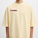 Camiseta com estampa frontal de frase estilizada e estampa traseira de urso com olhos em cruz, fundo de tinta respingada e símbolos de flechas e ferramentas.