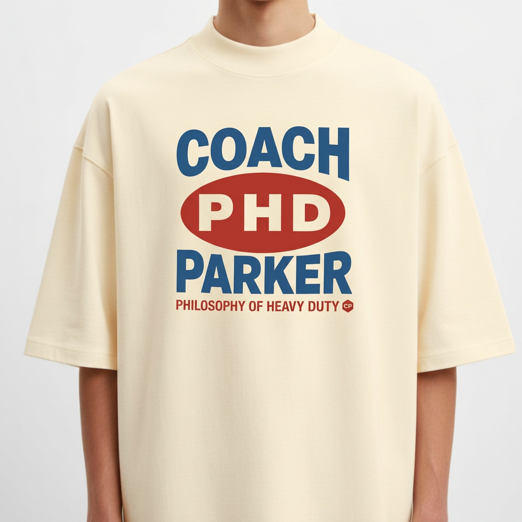 Camiseta com estampa frontal de texto estilizado com palavras "COACH PHD PARKER" em destaque, acompanhada de "PHILOSOPHY OF HEAVY DUTY" em menor tamanho.