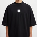 Camiseta com estampa frontal de pequeno texto no canto inferior e estampa traseira de onda imponente e sol vibrante em fundo quadriculado.