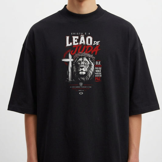 Camiseta com estampa frontal de um leão estilizado ao lado de uma cruz, acompanhada por textos destacados em diferentes tamanhos e fontes expressivas.