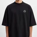 Camiseta com estampa frontal de pequeno símbolo circular com seta apontando para cima no lado esquerdo do peito e estampa traseira de surfista em túnel de onda dinâmica com efeitos de pinceladas.