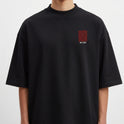 Camiseta com estampa frontal de barras verticais ao lado de caracteres pequenos e estampa traseira com caracteres grandes sobrepostos por caracteres menores.