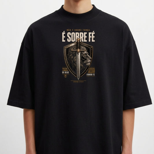 Camiseta com estampa frontal de escudo contendo uma espada centralizada e a imagem de um leão ao fundo, com textos ao redor enfatizando fé.