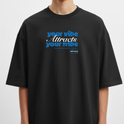 Camiseta com estampa frontal de texto estilizado "your vibe attracts your tribe" em letras grandes, acompanhada de pequenos detalhes textuais complementares.