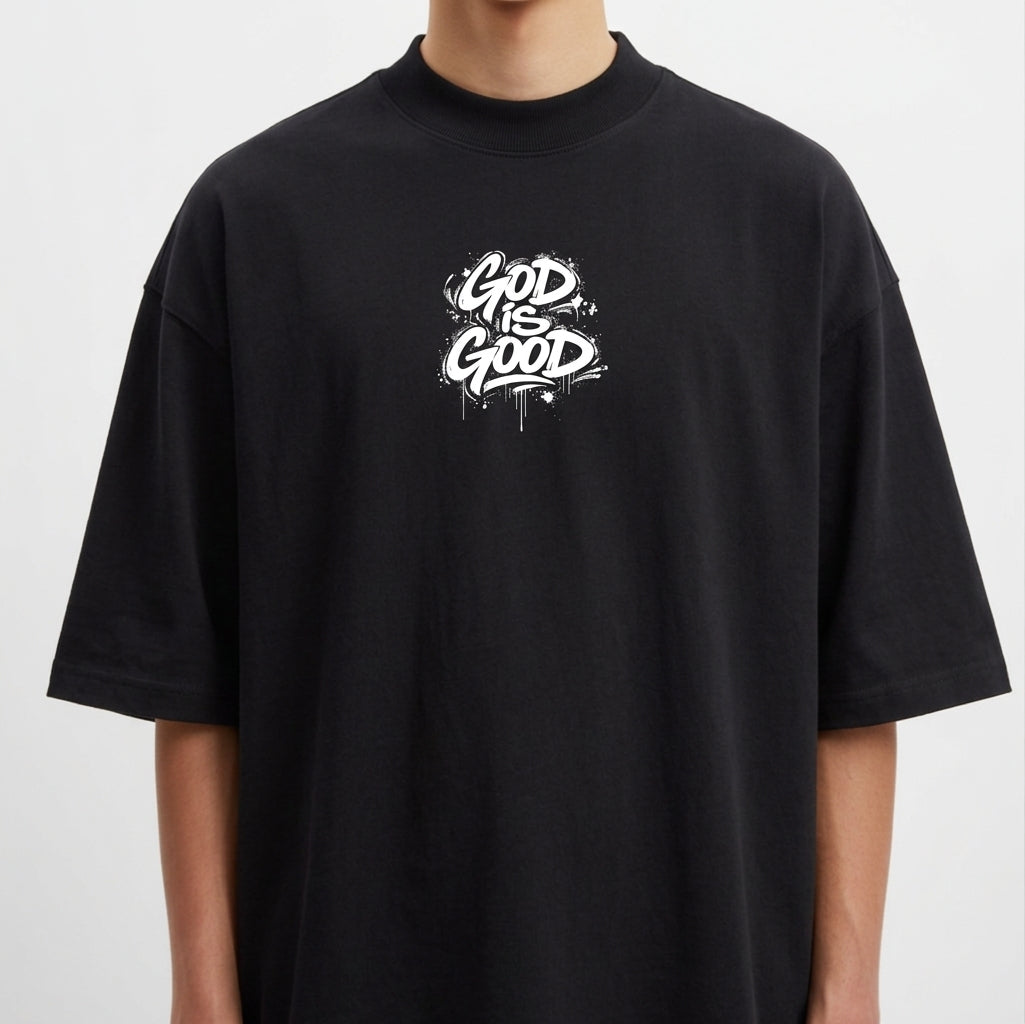 Camiseta com estampa frontal de lettering "God is Good" em estilo grafite e estampa traseira de crucifixo sobre a palavra "Jesus" e texto relacionado.
