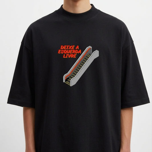 Camiseta com estampa frontal de escada rolante e frase "DEIXE A ESQUERDA LIVRE", em estilo tipográfico destacado ao lado da ilustração.