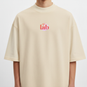 Camiseta com estampa frontal de "lab" em letras vibrantes e detalhes de linhas onduladas, e estampa traseira de "God is Good" sobrepondo um círculo.