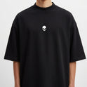 Camiseta com estampa frontal de caveira pequena e estampa traseira de pássaro em voo com texto estilizado por baixo, criando um contraste marcante.