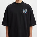 Camiseta com estampa frontal de “L5 2C” em estilo pixelizado e texto menor em roxo, e estampa traseira ampliada do mesmo texto com caracteres adicionais.