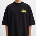 Camiseta com estampa frontal de "Blem Company" estilizado em tipografia mista e estampa traseira de uma cabeça clássica com rodelas de pepino nos olhos.