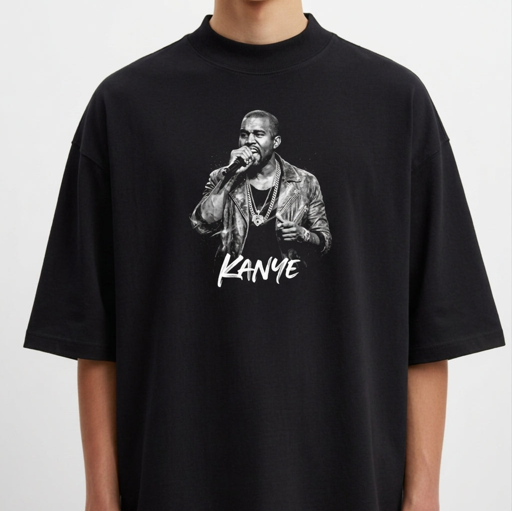 Camiseta com estampa frontal de um cantor segurando um microfone, vestindo jaqueta e colares, acompanhada pelo nome "Kanye" estilizado abaixo.