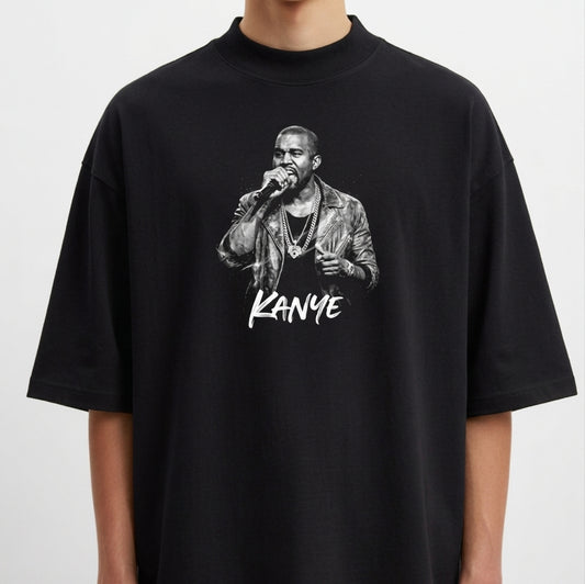 Camiseta com estampa frontal de um cantor segurando um microfone, vestindo jaqueta e colares, acompanhada pelo nome "Kanye" estilizado abaixo.