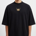 Camiseta com estampa frontal de cabeça de animal estilizada com dois olhos e estampa traseira de personagem em design geométrico acompanhada de textos e detalhes.