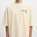 Camiseta com estampa frontal de texto estilizado ao lado de um símbolo estrelado e estampa traseira de logo similar ampliado com gráfico curvo dinâmico.