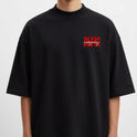 Camiseta com estampa frontal de texto estilizado em caixa vermelha e estampa traseira de retrato vintage com linhas verticais e texto cruzado.