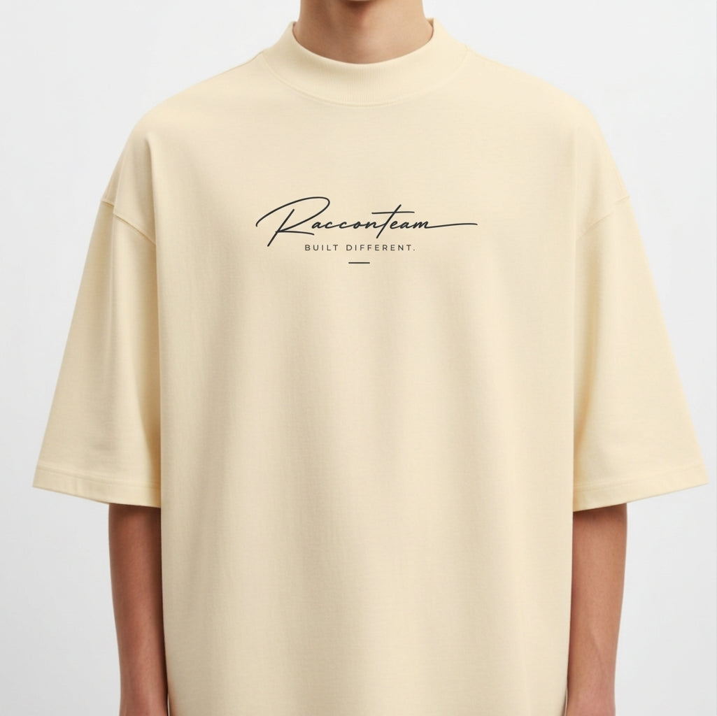 Camiseta com estampa frontal de lettering cursivo "Racoon Team - Built Different" e estampa traseira de iniciais grandes "RT", texto "Raccon Team - Est. 2017".