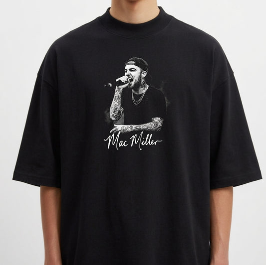 Camiseta com estampa frontal de um artista cantando no microfone, vestindo boné e camisa preta, destacando tatuagens nos braços e autógrafo abaixo.