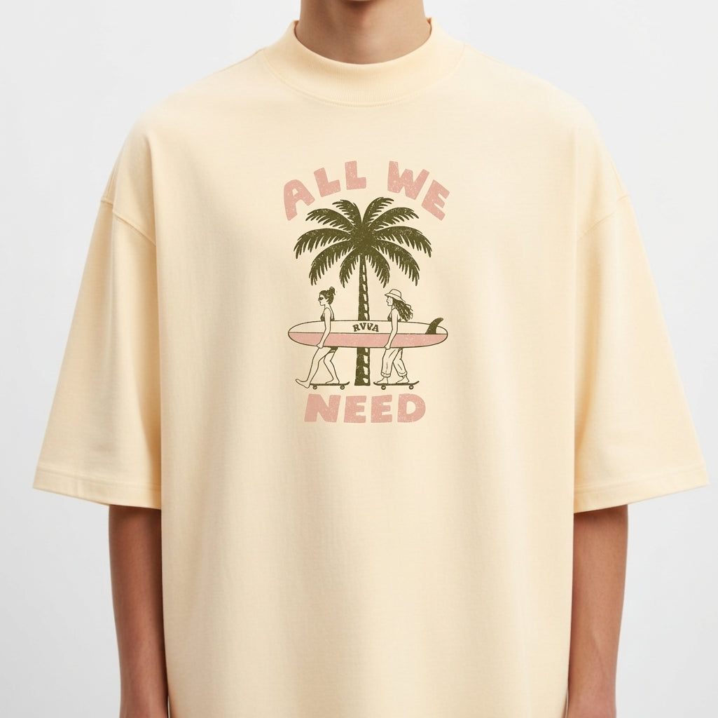 Camiseta com estampa frontal de duas pessoas carregando uma prancha de surfe diante de um coqueiro, acompanhada pela frase "ALL WE NEED".