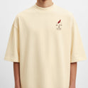 Camiseta com estampa frontal de caracteres japoneses e uma pena vermelha estilizada e estampa traseira de figura alada centralizada com elementos geométricos.