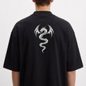 Camiseta com estampa frontal de assinatura estilizada delicada e estampa traseira de dragão tribal detalhado com asas curvas e cauda serpenteante.
