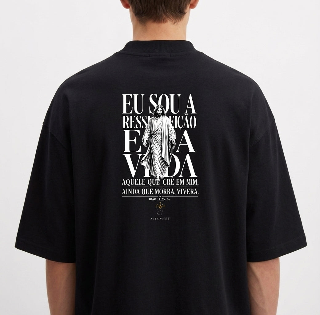 Camiseta com estampa traseira de uma figura central religiosa e frase que menciona ressurreição e vida, cercada por texto estilizado.