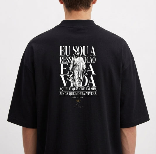Camiseta com estampa traseira de uma figura central religiosa e frase que menciona ressurreição e vida, cercada por texto estilizado.