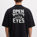 Camiseta com estampa frontal de "LUNOVA" em letras grandes e efeito desgastado, e estampa traseira de um olho detalhado entre "OPEN YOUR EYES".