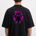 Camiseta com estampa frontal de inscrição estilizada e estampa traseira de urso sorridente com olhos em forma de "X" sobre fundo de respingos vibrantes.