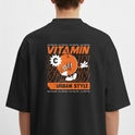 Moletom com estampa traseira de personagem laranja estilizado segurando uma flor, rodeado por repetição da palavra "VITAMIN" e texto "URBAN STYLE".