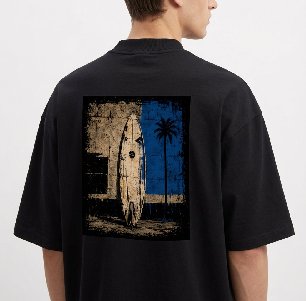 Camiseta com estampa frontal de logotipo minimalista e estampa traseira de prancha de surf encostada em parede desgastada com palmeira e fundo geométrico.