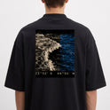 Camiseta com estampa frontal de símbolo minimalista em forma de flecha e estampa traseira de fotografia de oceano com coordenadas no rodapé.