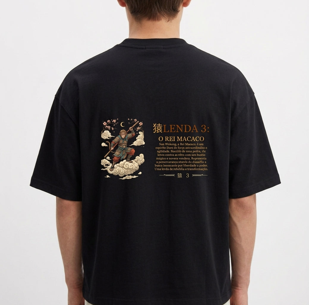 Camiseta com estampa frontal de um emblema dourado com uma coroa, texto "O Rei Macaco (Sun Wukong)" e estampa traseira de uma ilustração detalhada com "Lenda 3: O Rei Macaco".