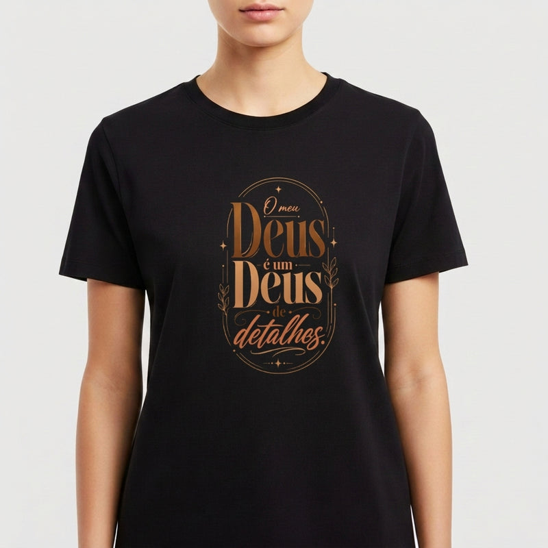 Camiseta com estampa frontal de texto estilizado "O meu Deus é um Deus de detalhes" e estampa traseira com pequeno logotipo "Santa Veste" acima de cruz.